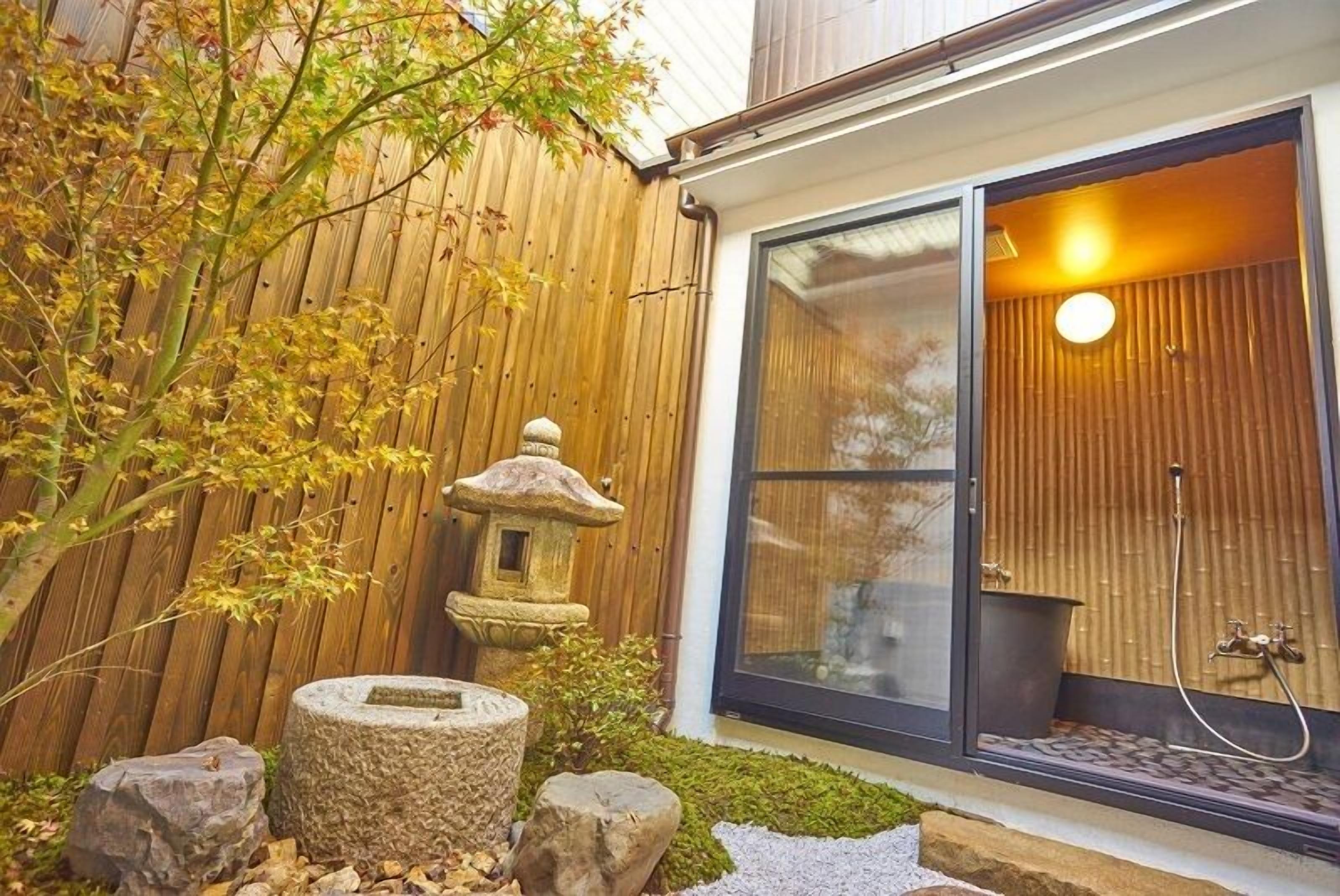 A wooden fence, a stone lantern, and a glass door leading to a room with a bamboo wall and a shower.