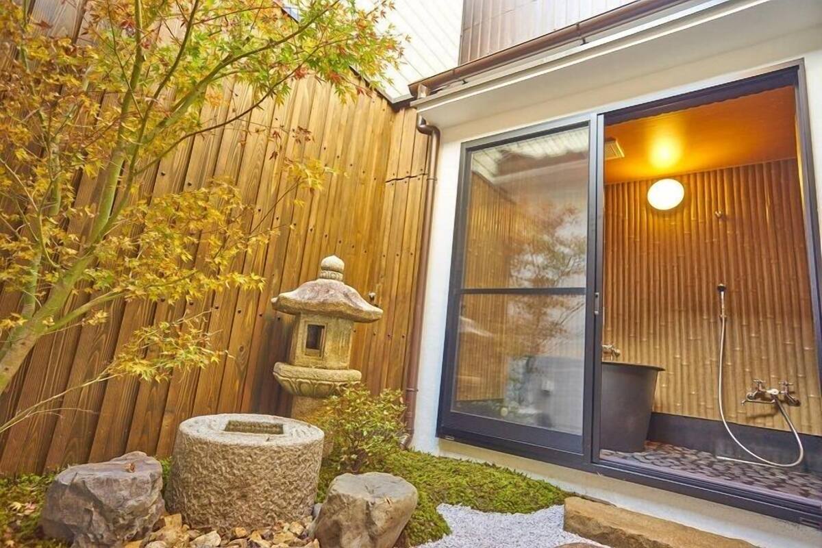 A wooden fence, a stone lantern, and a glass door leading to a room with a bamboo wall and a shower.