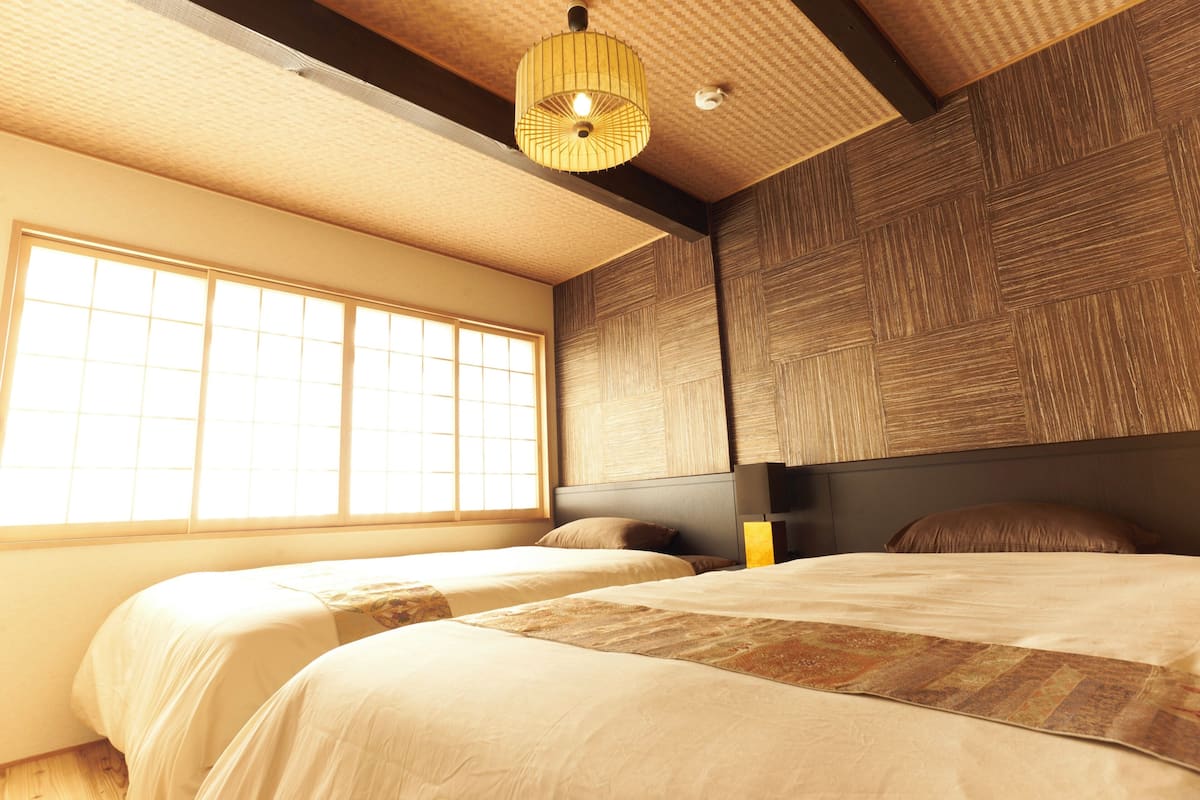 A bedroom with two beds, a large window, and a ceiling light fixture.