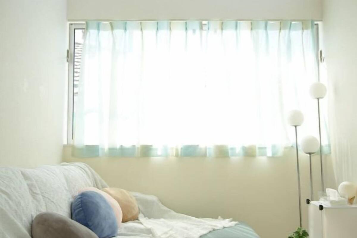 A room with a bed, a window with curtains, and a floor lamp.