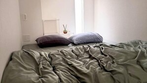 A bed with green bedding, a window, and a small table with a candle. - Only 10 minutes by train to Asakusa & Skytree! (Tokyo)