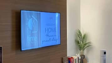 Una TV a schermo piatto montata a parete mostra un messaggio di benvenuto e un orologio.