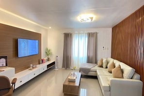 A modern living room with a flat-screen TV, a sofa, a coffee table, and a wooden accent wall. - Time To Sleep — Casa Ala Una (Butuan)