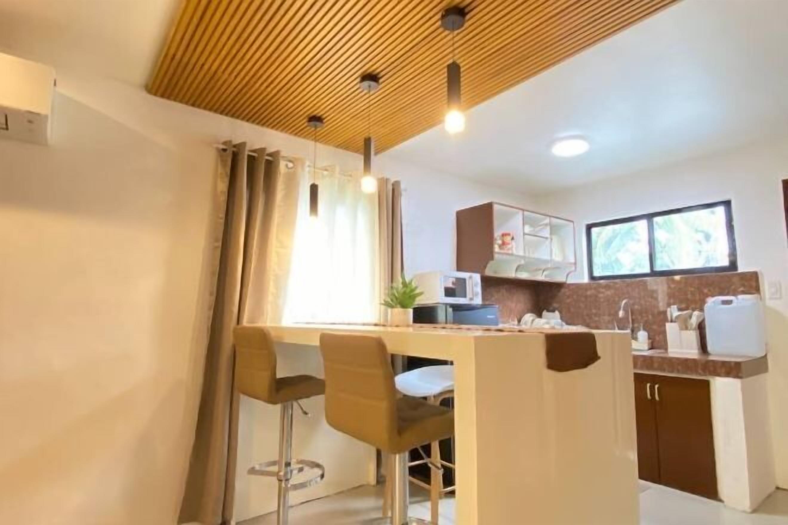 A modern kitchen with a wooden ceiling, a bar area with stools, and a window providing natural light.