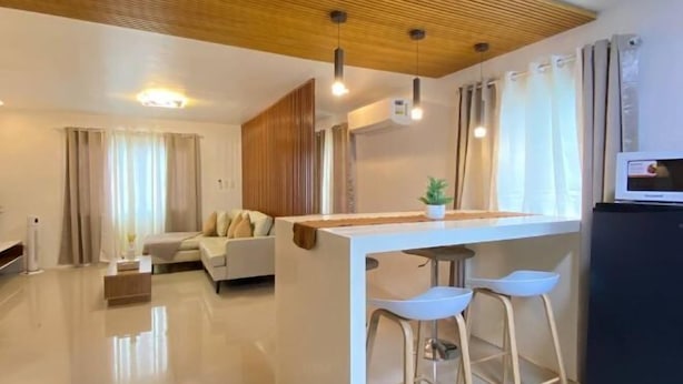 A modern living room with a sofa, a dining area with stools, a wooden ceiling, and a flat-screen TV. - Time To Sleep — Casa Ala Una (Butuan)