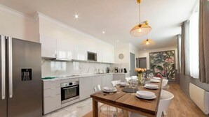 A modern kitchen with white cabinets, a stainless steel refrigerator, and a wooden dining table set for six. - Spacious 170m² Apartment with AC - Paris Bercy (Paris)