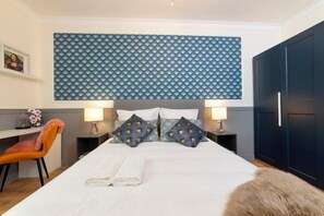 Une chambre d’hôtel comprenant un lit, deux tables de chevet, une chaise, une armoire et une tête de lit ornée d’un motif géométrique.