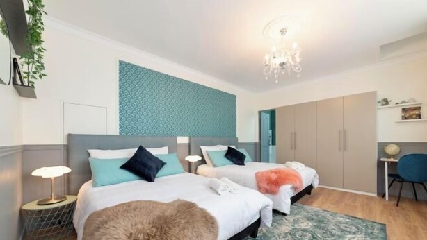 Een moderne slaapkamer met twee bedden, een kroonluchter, een behang met patroon en een klein bureau met stoel.