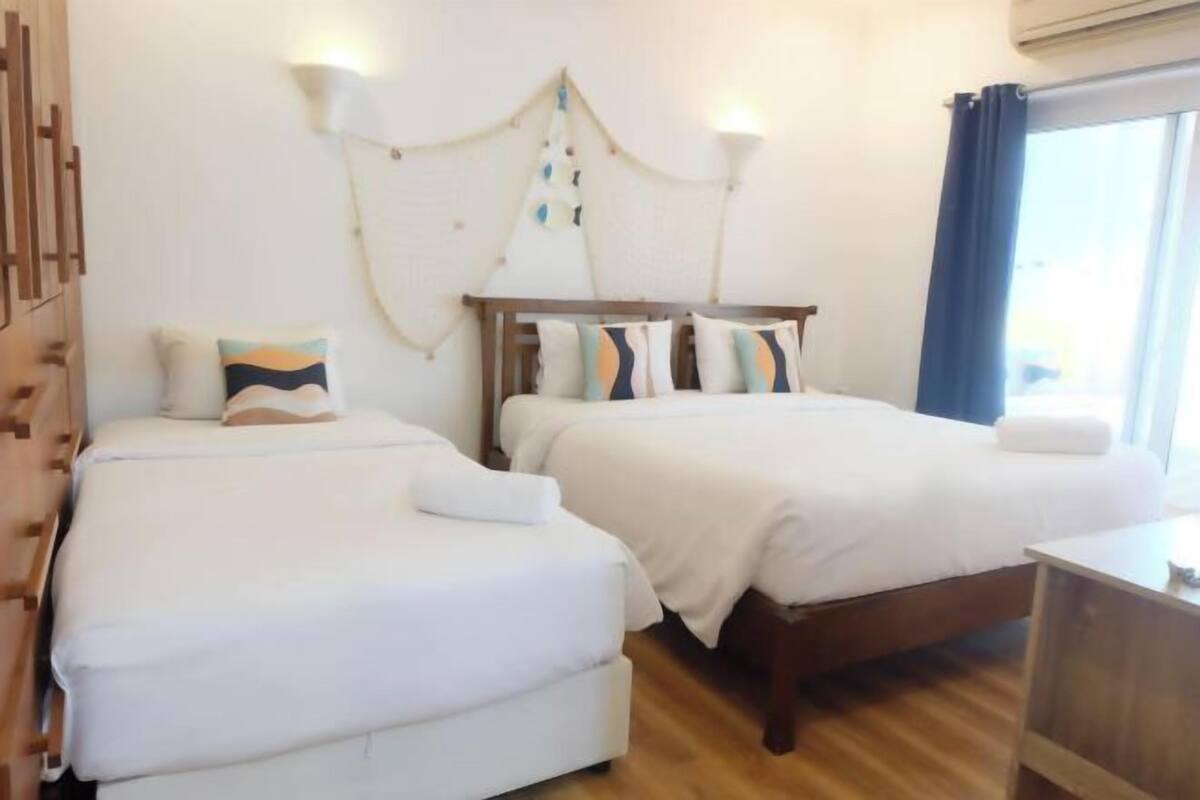 Habitación de hotel con dos camas, cabecero de madera, un escritorio pequeño y una ventana con cortinas.