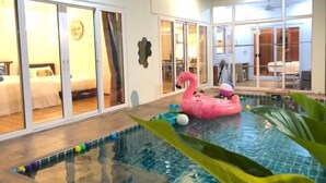 A hotel room with a pool, a pink flamingo float, and a bed with a white headboard.