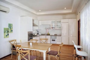 Un coin repas avec une table et des chaises en bois, une cuisine en arrière-plan et des meubles de rangement blancs.
