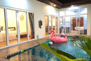 A swimming pool with a pink flamingo float, indoor sliding doors, and a bed visible through the glass doors. - The Pool House Pattaya No.9 - 3 bedroom (Pattaya)