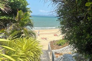 Une plage avec vue sur la mer, un sentier en pierre menant au rivage, le tout entouré de verdure.