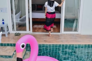 Ein Zimmer mit einer Glasschiebetür, die auf einen Balkon führt, einem rosa aufblasbaren Flamingo und einem gefliesten Poolbereich.