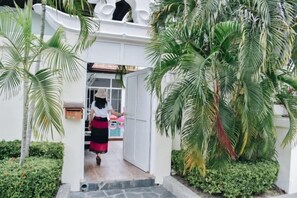 A person walking through a white archway into a building surrounded by greenery. - The Pool House Pattaya No.9 - 3 bedroom (Pattaya)
