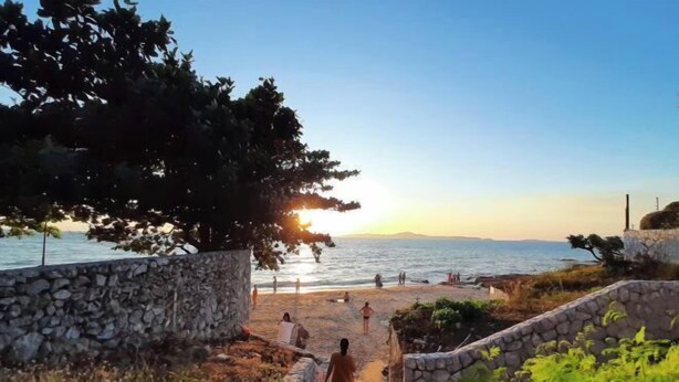 A stone pathway leading to a beach with people walking and sitting.