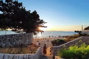 Un sendero de piedra que lleva a una playa con gente caminando y sentada.