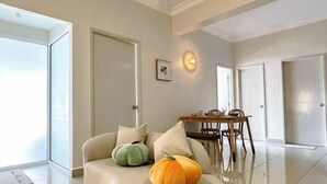 Een moderne woonkamer met een bank, twee decoratieve pompoenen, een eettafel met stoelen en een wandlamp.