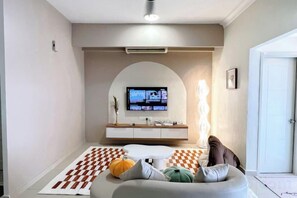 Un salon avec un téléviseur, un canapé, un tapis à motifs et une porte blanche.