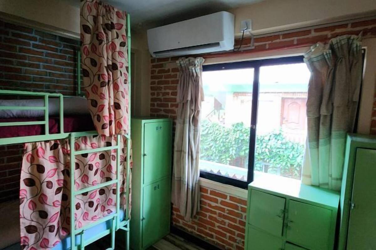 A room with a bunk bed, a window with curtains, a brick wall, and an air conditioning unit.