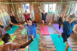 Un groupe de personnes se trouve dans une pièce aux murs de briques et aux grandes fenêtres, et participe à un cours de yoga.