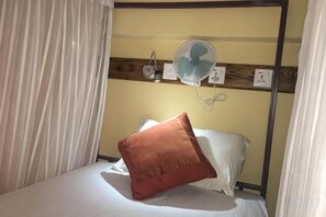 A single bed with a white pillow and a red pillow, a bedside fan, and a power outlet on the wall. - Kiwi Backpackers Hostel Pokhara (Pokhara)