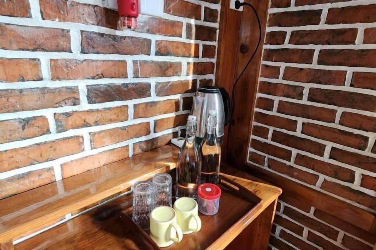 A wooden tray with mugs, a kettle, and bottles on a brick wall.