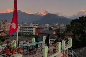 Une terrasse sur le toit, avec des tables et des chaises, un drapeau et une vue sur les montagnes.
