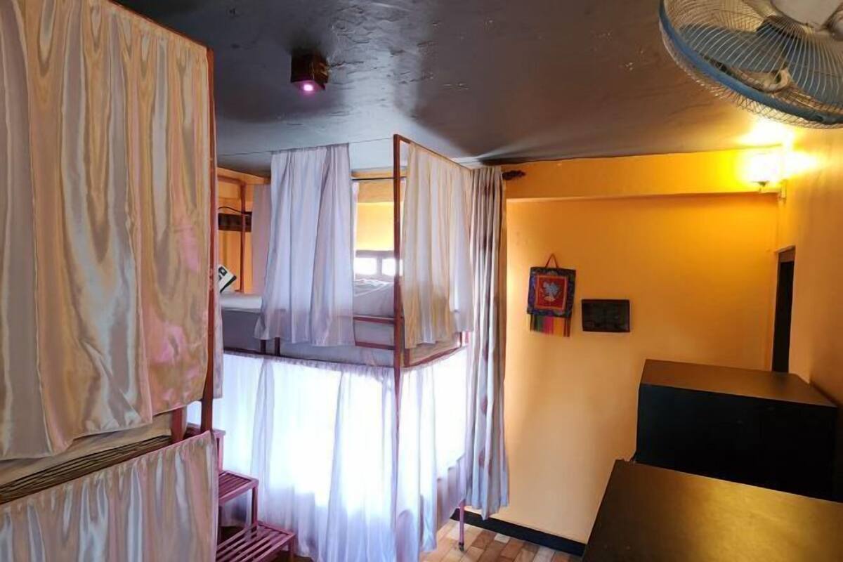 A room with a bunk bed, a standing fan, a small table, and a wall-mounted shelf.