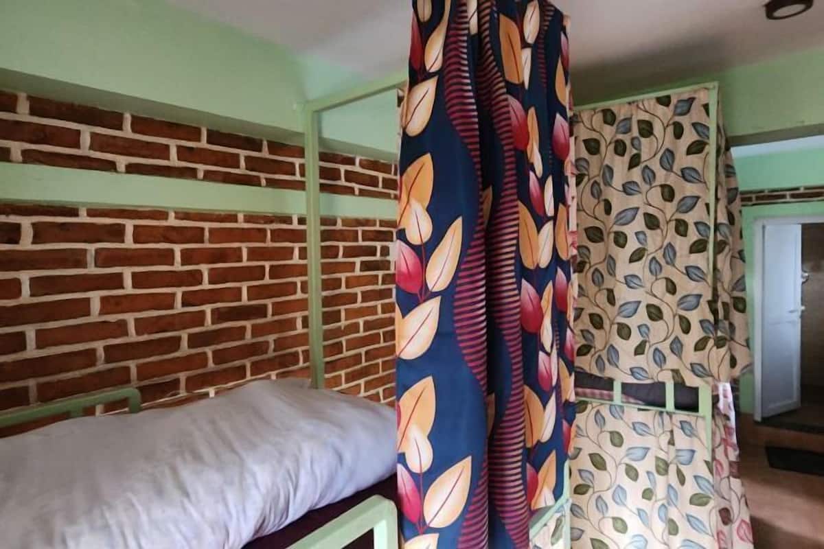 A room with a brick wall, a bed with a green frame, and patterned curtains.