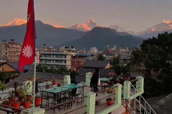 A rooftop terrace with tables and chairs, a flag, and a view of mountains.