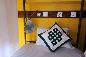 Una cama litera con un ventilador, un enchufe y una almohada decorativa.