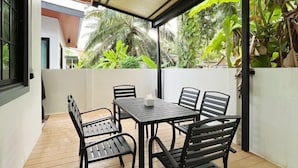 A covered outdoor seating area with a table and chairs, surrounded by lush greenery and a view of palm trees. - DelZiaNa Bara Villa Pakbara Satun (La-ngu)