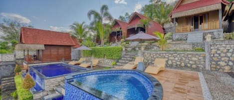 Un complejo turístico con piscina, terraza de madera y edificios con techo de paja.
