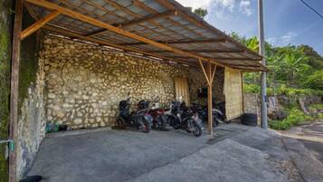A covered motorcycle parking area with a stone wall and a metal roof.