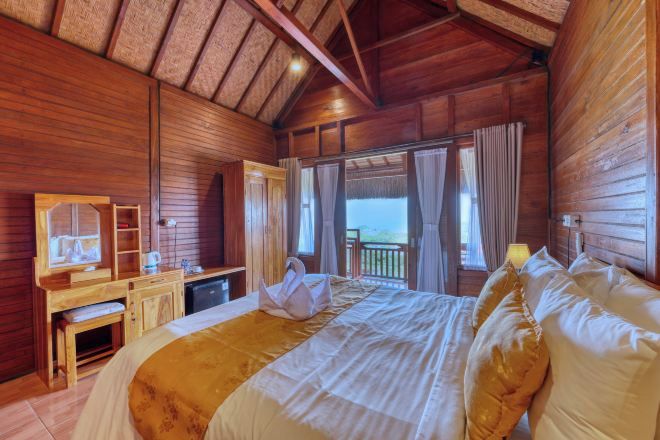 Una habitación de madera con una cama, un escritorio, un espejo y vistas al exterior.