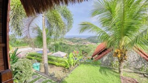 A view from a balcony with a thatched roof, palm trees, and a patterned pathway leading to a door. - Sebuluh Sunset Hill (Bali)