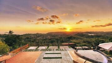 A sunset view from a terrace with a pool, surrounded by lush greenery.
