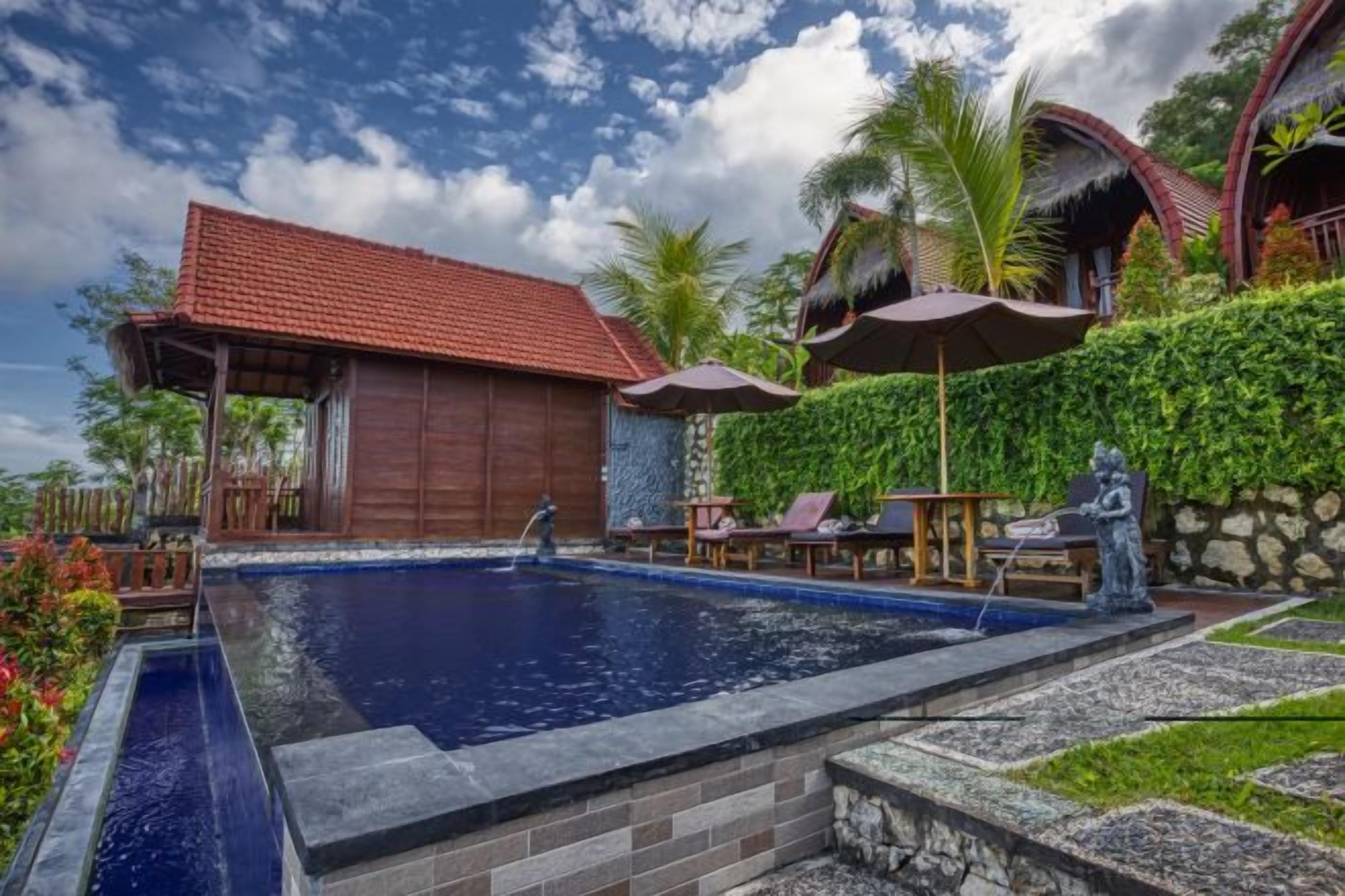 A swimming pool with a wooden structure and lounge chairs, surrounded by greenery and a clear sky.