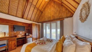 A bedroom with a wooden ceiling, a bed with white and gold bedding, a desk with a computer, and a large window. - Sebuluh Sunset Hill (Bali)