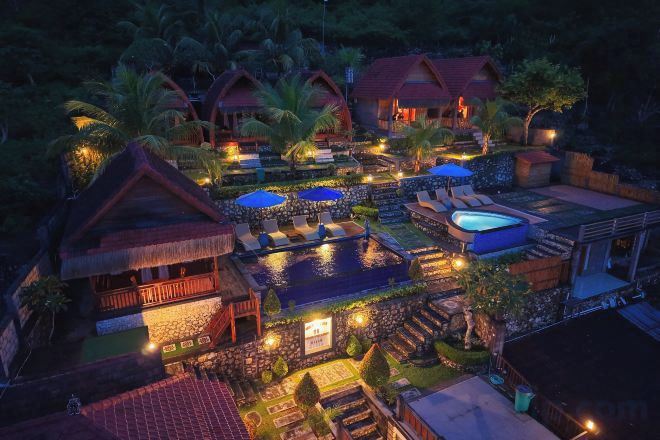 Een resort met meerdere bungalows boven het water, een zwembad en een goed verlicht buitengebied.