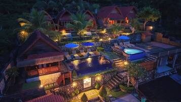 Een resort met meerdere bungalows boven het water, een zwembad en een goed verlicht buitengebied.