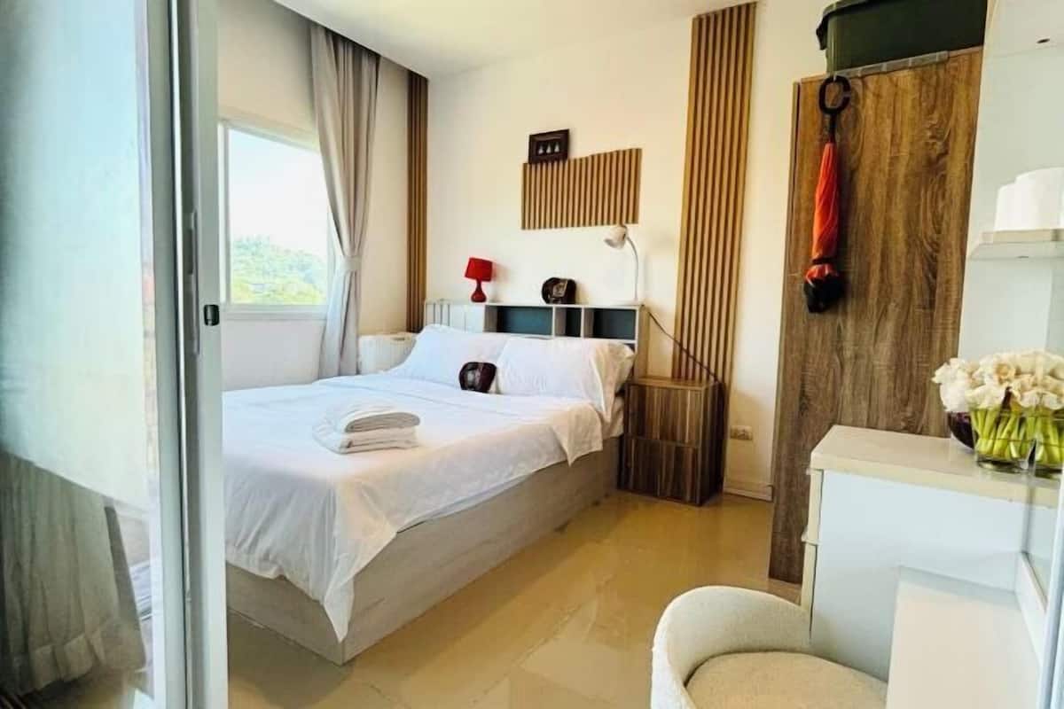 A bedroom with a bed, a bedside table, a lamp, a wooden panel, and a chair.