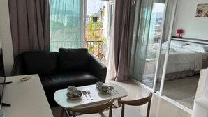 Una camera d'albergo con un divano in pelle nera, un tavolo da pranzo con piatti e posate, e un letto con biancheria bianca.