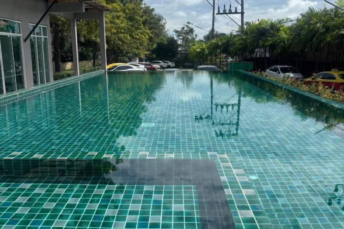 A swimming pool with a tiled floor, surrounded by parked cars and greenery.