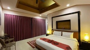A hotel room with a large bed, a ceiling fan, a desk with a chair, and a nightstand with a lamp. - The Iris Pool Villa (Chalong)