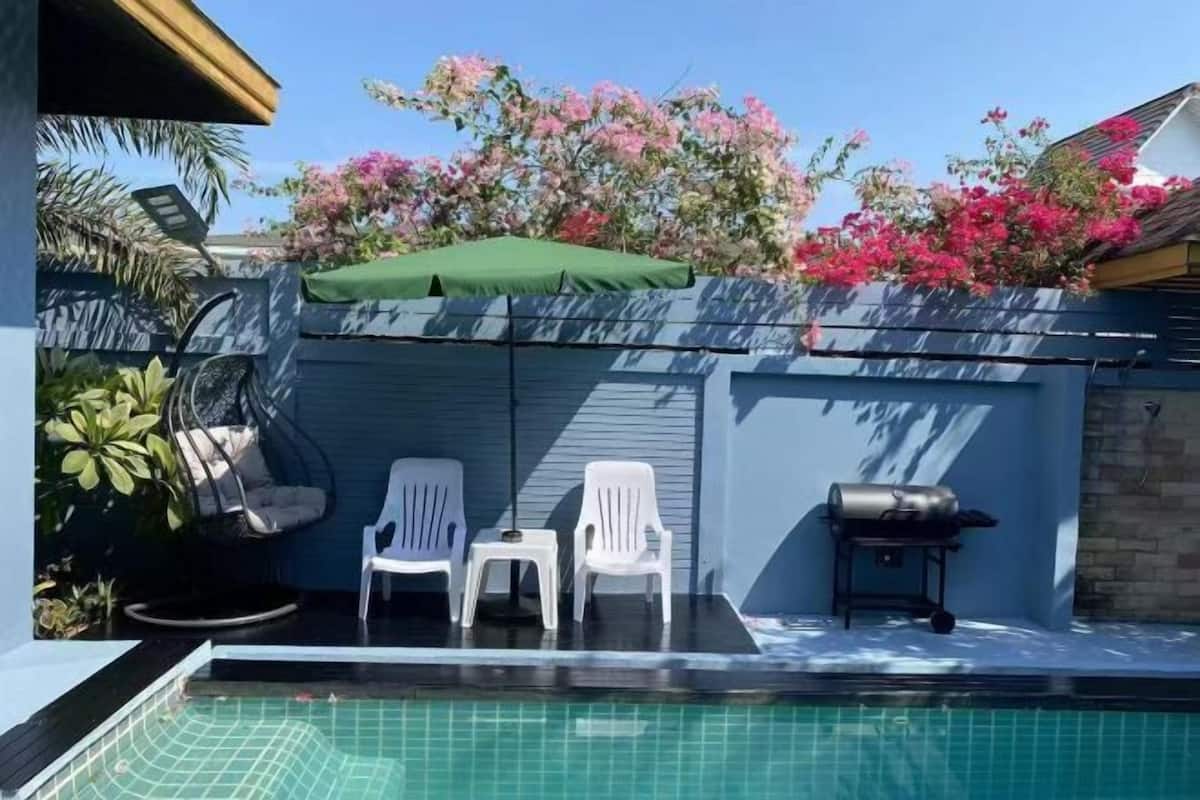 A swimming pool with two white chairs, a hanging chair, and a barbecue grill.