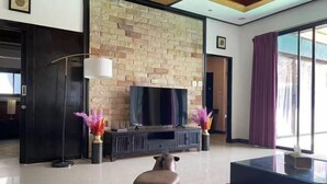 A modern living room with a stone wall, a flat-screen TV, a sofa, and two decorative vases. - The Iris Pool Villa (Chalong)