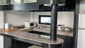 A modern kitchen with a central island, stainless steel appliances, and black cabinetry. - The Iris Pool Villa (Chalong)