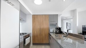 A modern kitchen with a granite countertop, stainless steel appliances, and wooden cabinets. - Arcade in the Sky - Views, Games & Vibes (Brisbane)